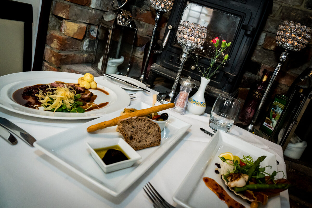 A table laid with a main course and a glass of red wine against exposed brickwork.